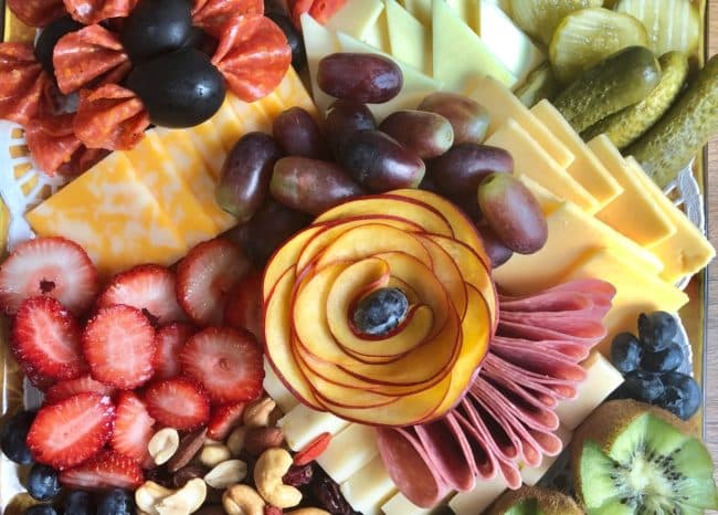 Strawberries, green grapes and assorted cheeses on a wooden cheese tray with two glasses of red wine