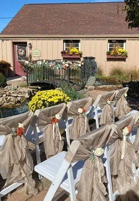 White chairs with taupe sashes with rust and ivory flowers sitting in a garden