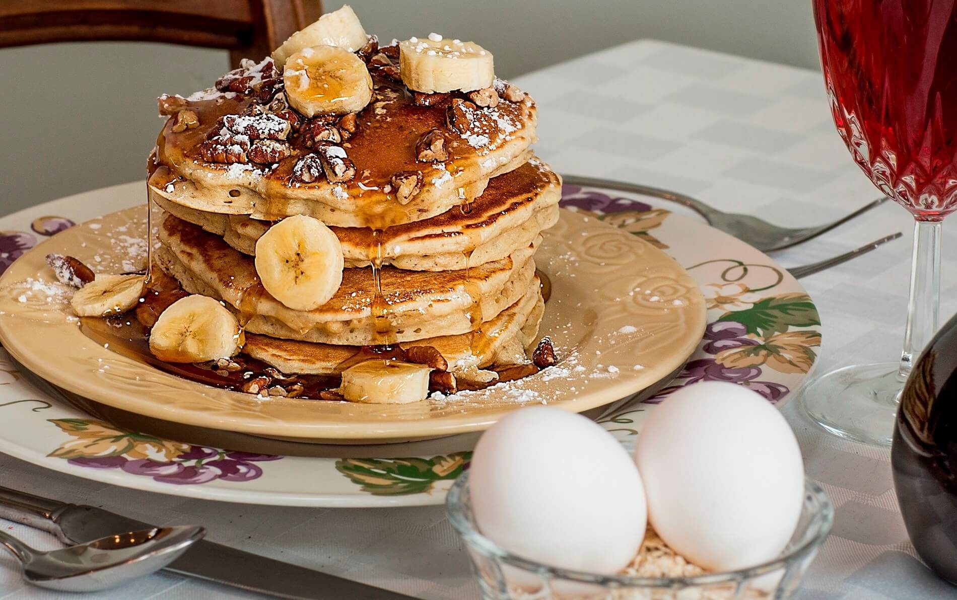 Four pancakes topped with bananas, pecans and syrup