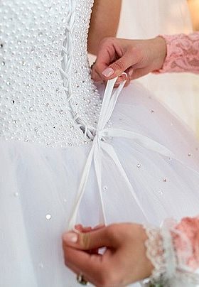 Bride in white getting her dress tied in the back