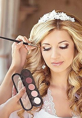 Bride with blonde hair and white heading getting assistance with her make up preparation