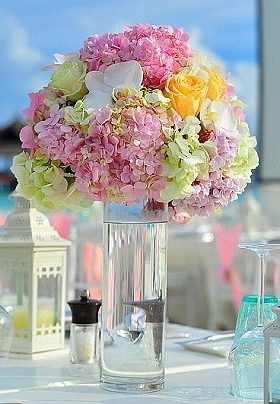 Table set with clear vase with pale pink and yellow roses and white lanterns as a centerpiece