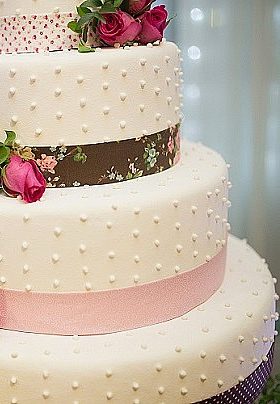 Three layer white wedding cake with pink flowers and brown and pink ribbon trim