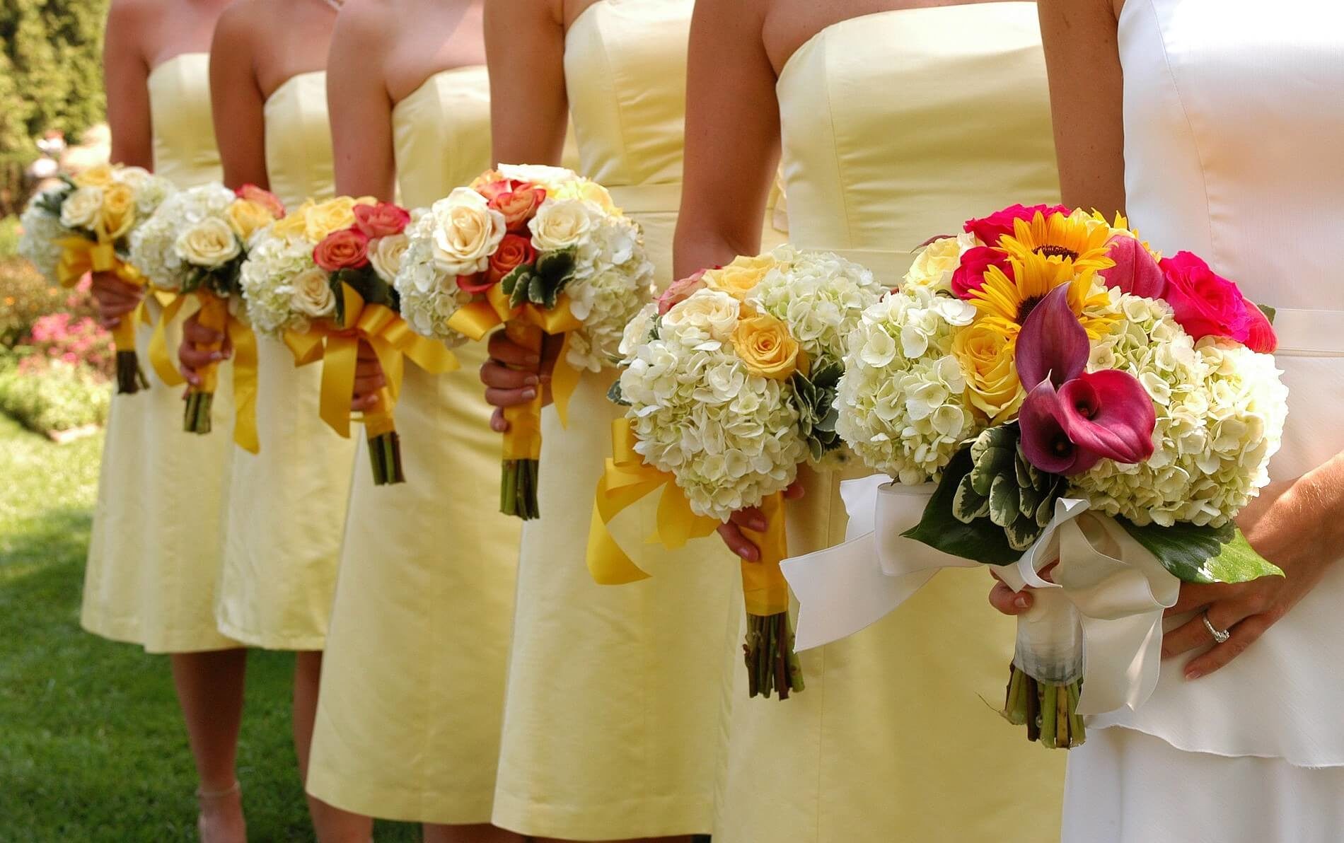 Bride in white dress with 5 bridesmaids in yellow dresses all with orange and yellow rose bouquets