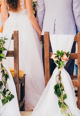 Bride and Groom standing in front of chairs decorated with white ribbon and pink flowers