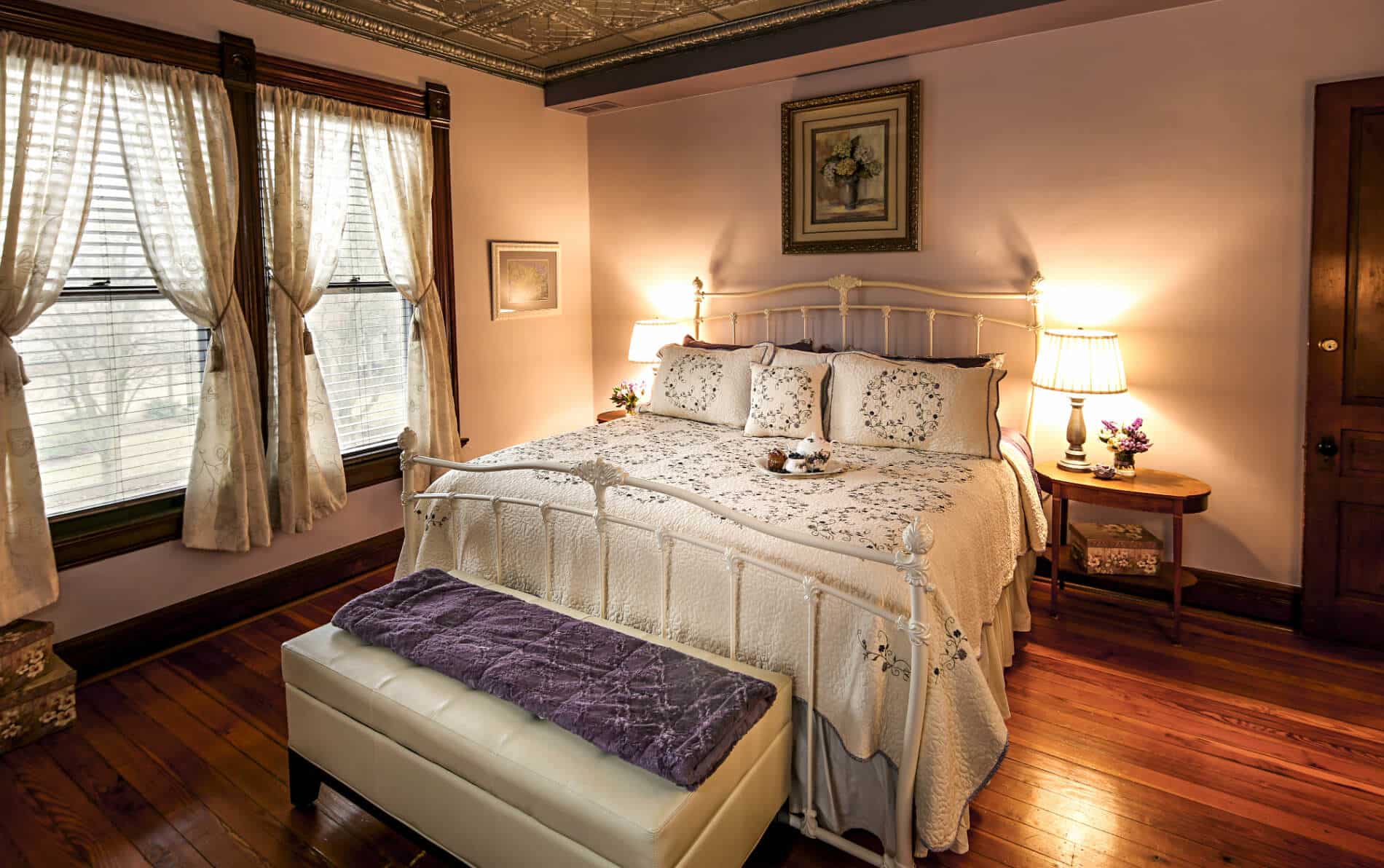 White bed with pink floral quilt, wicker table and tub for two with lit candles, strawberries and glasses of champagne