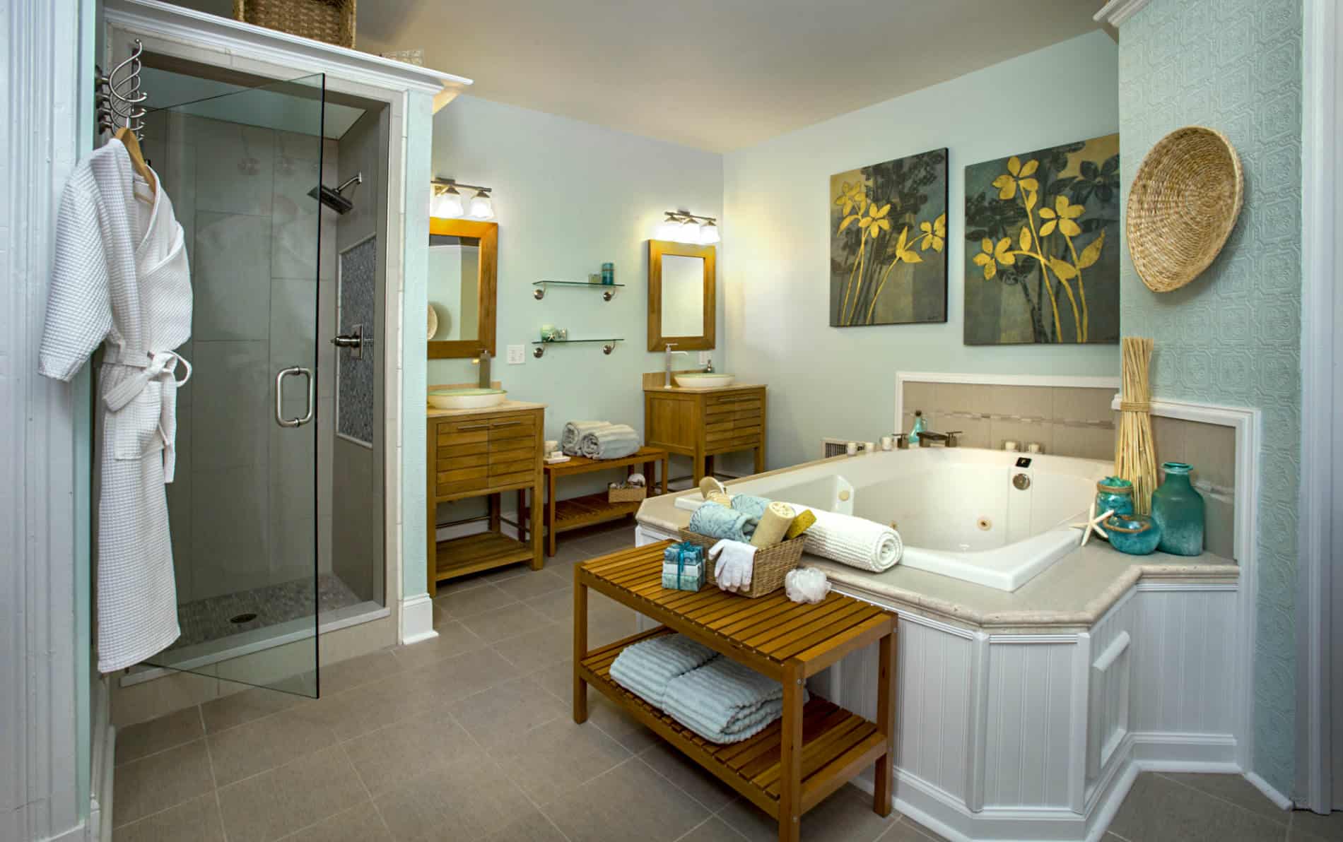 Room with large white tub, two wooden sink stands with green glass washbowls, pale green walls, and two wooden benches