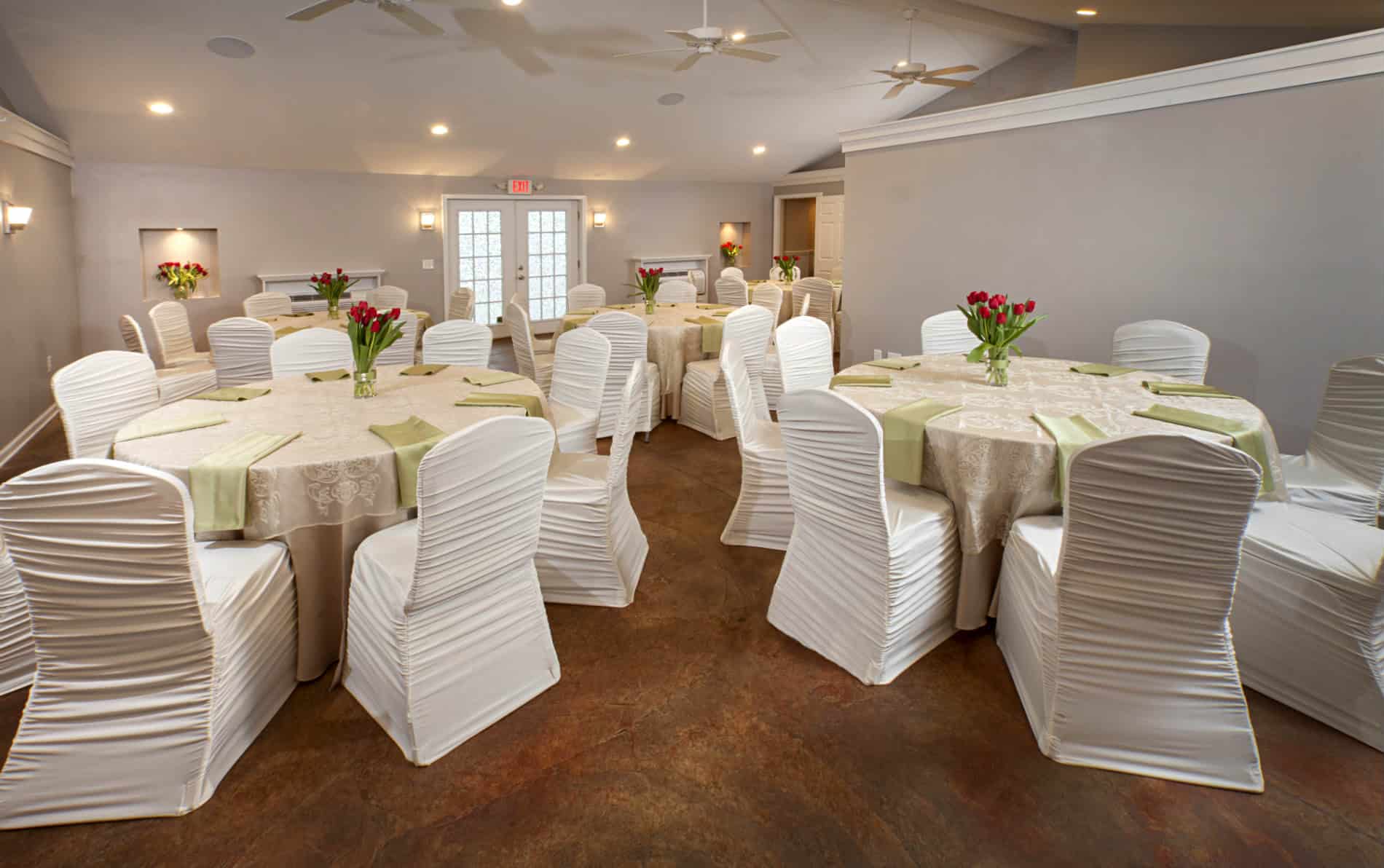 Large open room with four off - white lace covered tables, pale green napkins and red tulip arrangements
