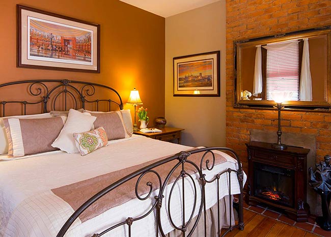 Bedroom with wraught iron bed, artwork on walls. Fireplace and mirror above fireplace.