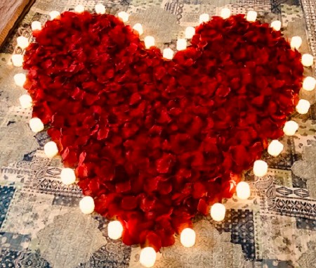 Red heart shaped rose petals surrounded by lit white candles