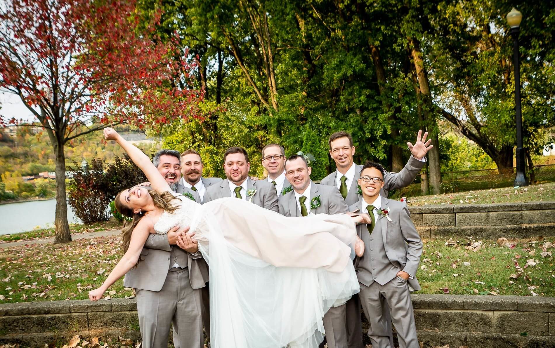 Bride with hands in the air being held horizontally by seven men