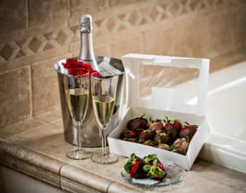 Silver bucket with a bottle of champagne, two glasses of champagne and a white box with chocolate covered strawberries