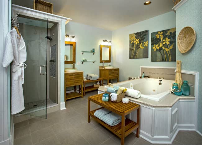 Room with large white tub, two wooden sink stands with green glass washbowls, pale green walls, and two wooden benches