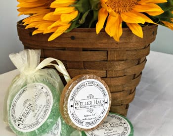 Brown woven basket with four large yellow sunflowers and packaged green and orange round soaps