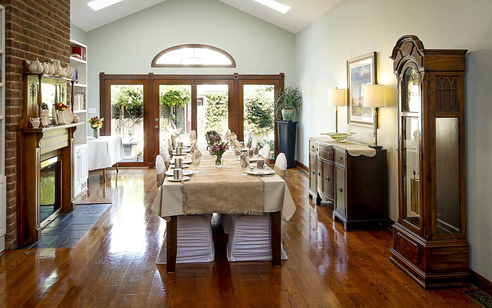 Long dining room with hardwood floors, extra long dining table with tan tablecloth and white covered chairs