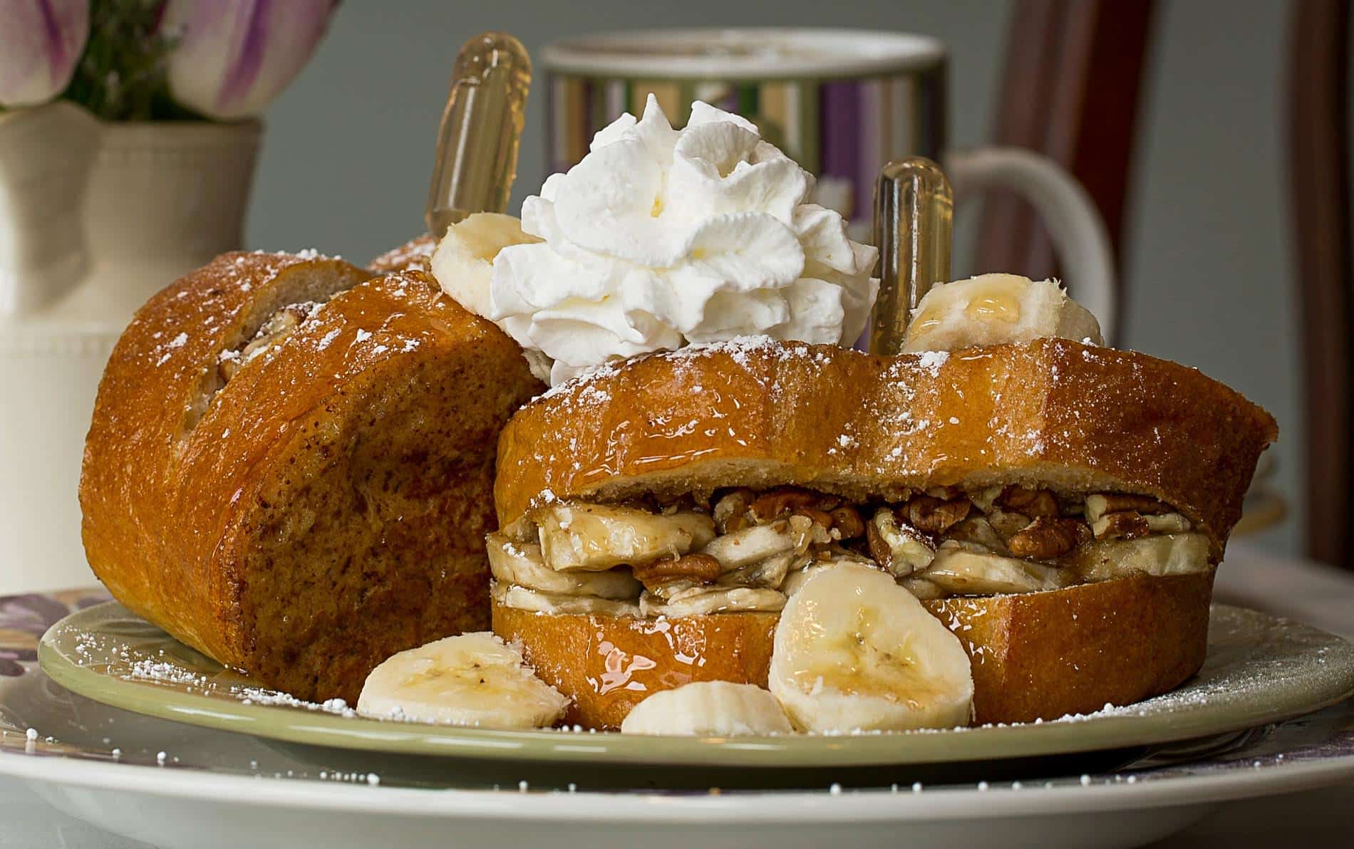 Two pieces of french bread stuffed with bananas and pecans topped with whipped cream