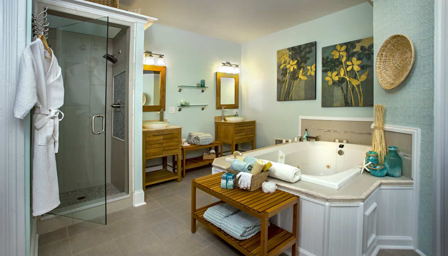 Room with large white tub, two wooden sink stands with green glass washbowls, pale green walls, and two wooden benches