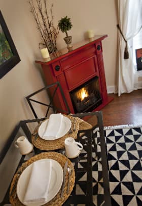 Red fireplace with burning fire next to a black iron breakfast table with two white place settings.