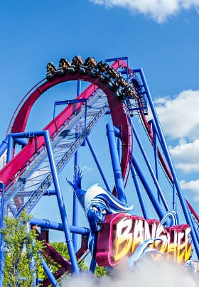Blue and red roller coaster with eight cars of people riding upside down with a bright blue sky background