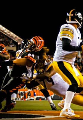 Teams playing football, one player in orange and black being tackled and another in yellow and black throwing the football