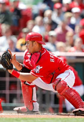 Male baseball player with white pants, red knee pads and helmet, red shirt and black glove catching a baseball