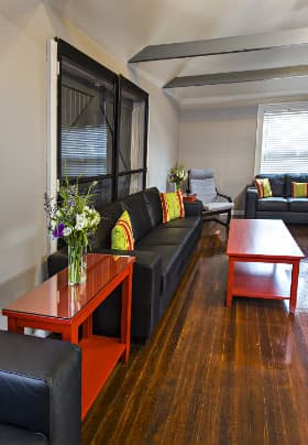 Large room, hardwood floors, black chairs and couches, red tables, red-green-blue-yellow-orange striped pillows, gray ceiling beams