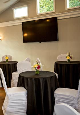 Meeting room with cathedral ceilings, three horizontal windows and three black tables and white covered chairs