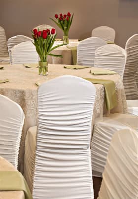 Round tables with tan lace table cloths, white covered chairs and an arrangement of red tulips on the table