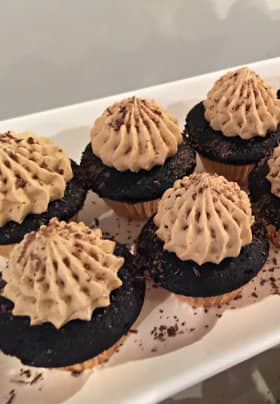 White rectangular plate with seven small chocolate cupcakes with chocolate icing sprinkled with pieces of shaved chocolate