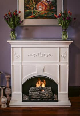 Brown wood fireplace with burning orange and yellow fire with a vase of yellow and pink flowers on mantel