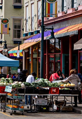 Multi-colored four-story buildings with a blue tent in front containing fresh green lettuce and red vegetables