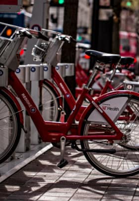 Red bicycles parked in a silver bicycle rack along a brick paved sidewalk