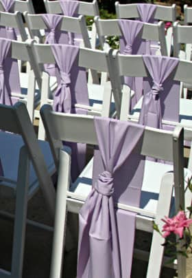 Four rows of white chairs decorated with a pale purple bow tied to the back of the chair