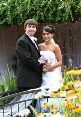 Bride with purple flower arrangement and groom standing on an iron bridge in front of yellow flowers