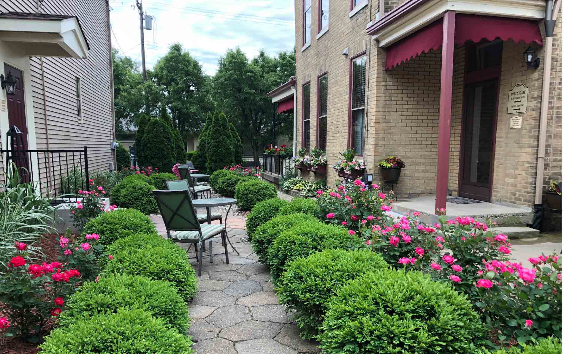 Exterior view between properties featuring a small sitting area and a plethora of colorful flowers. 