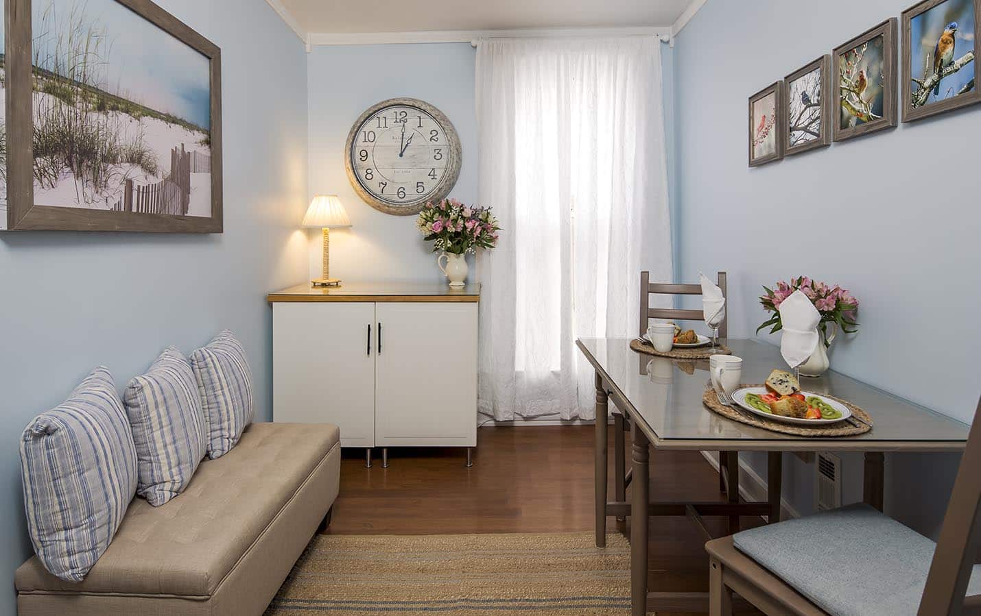 Setting area with a tan padded Bench, table for 2, and large clock on the wall