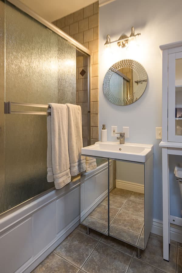 Standard bathtub with sliding glass doors, mirrored vanity with round mirror on the wall