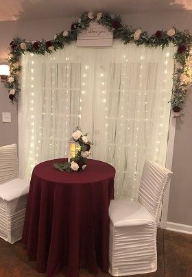 Table for two with burgundy table cloth and lighted white curtain background