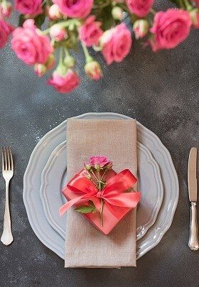 White plates with silverware topped with peach napkin wrapped in a peach bow