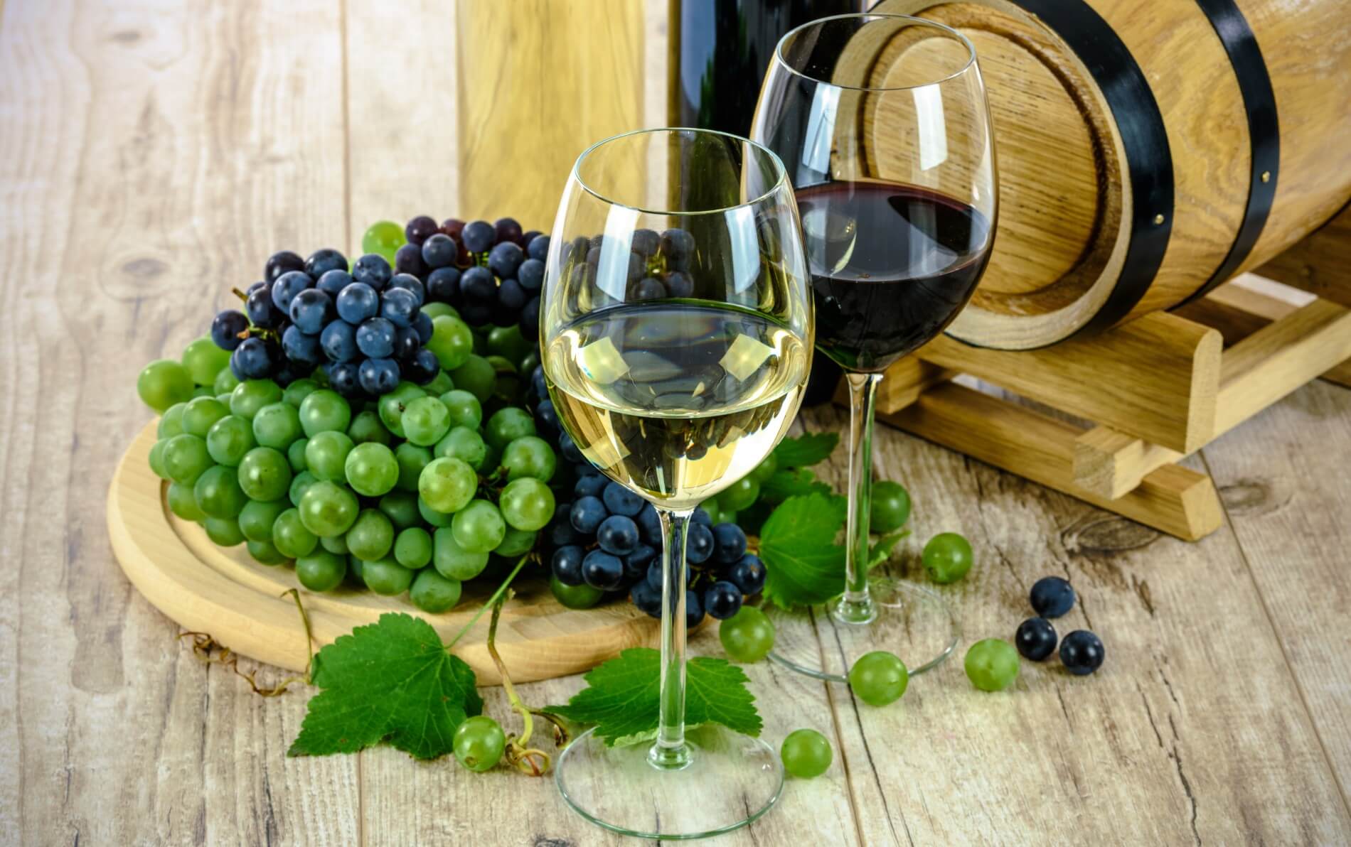 Wooden table with purple and green grapes near a glass of white wine and red wine